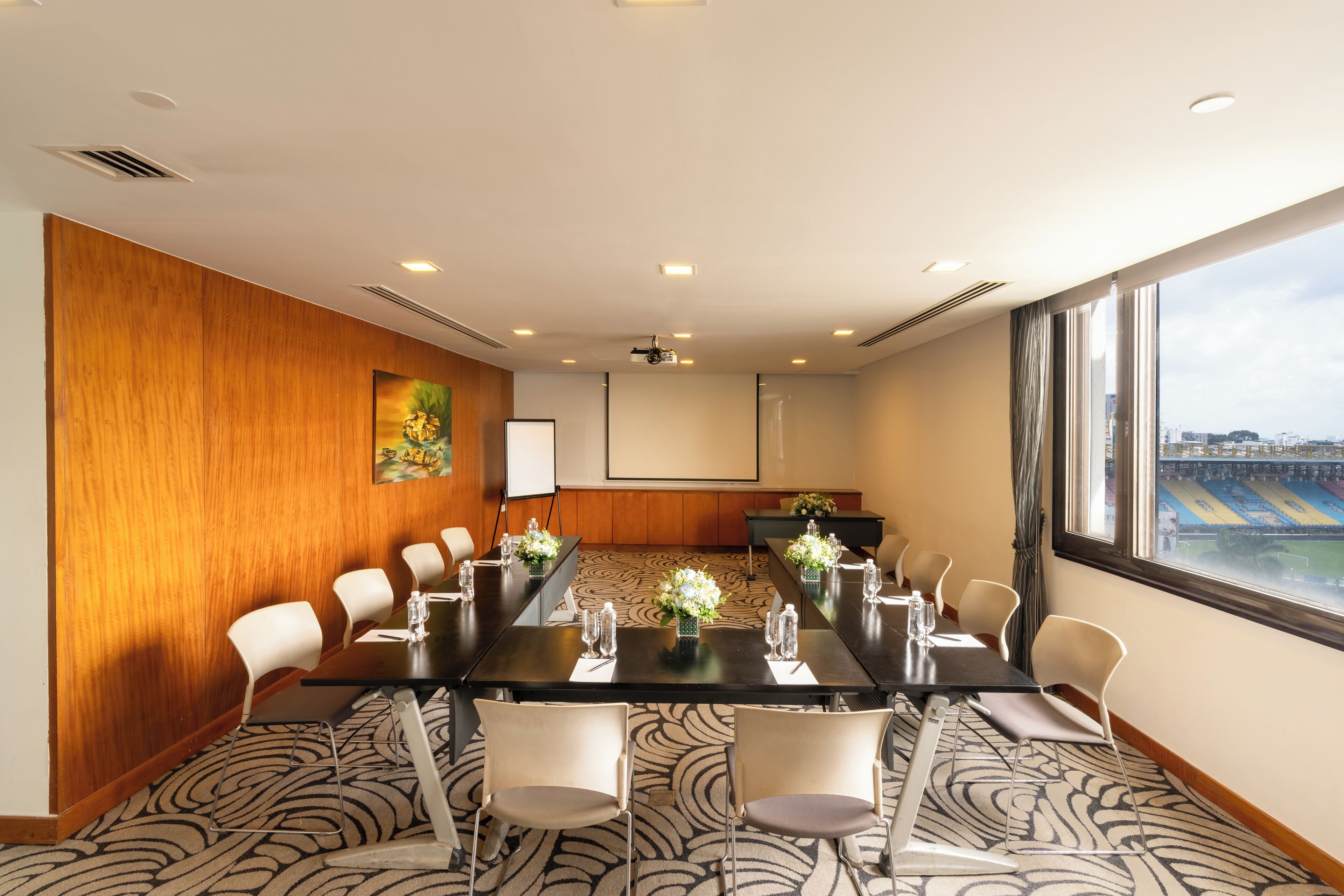 A conference room with a long table, chairs, and a large window with a view of a stadium.