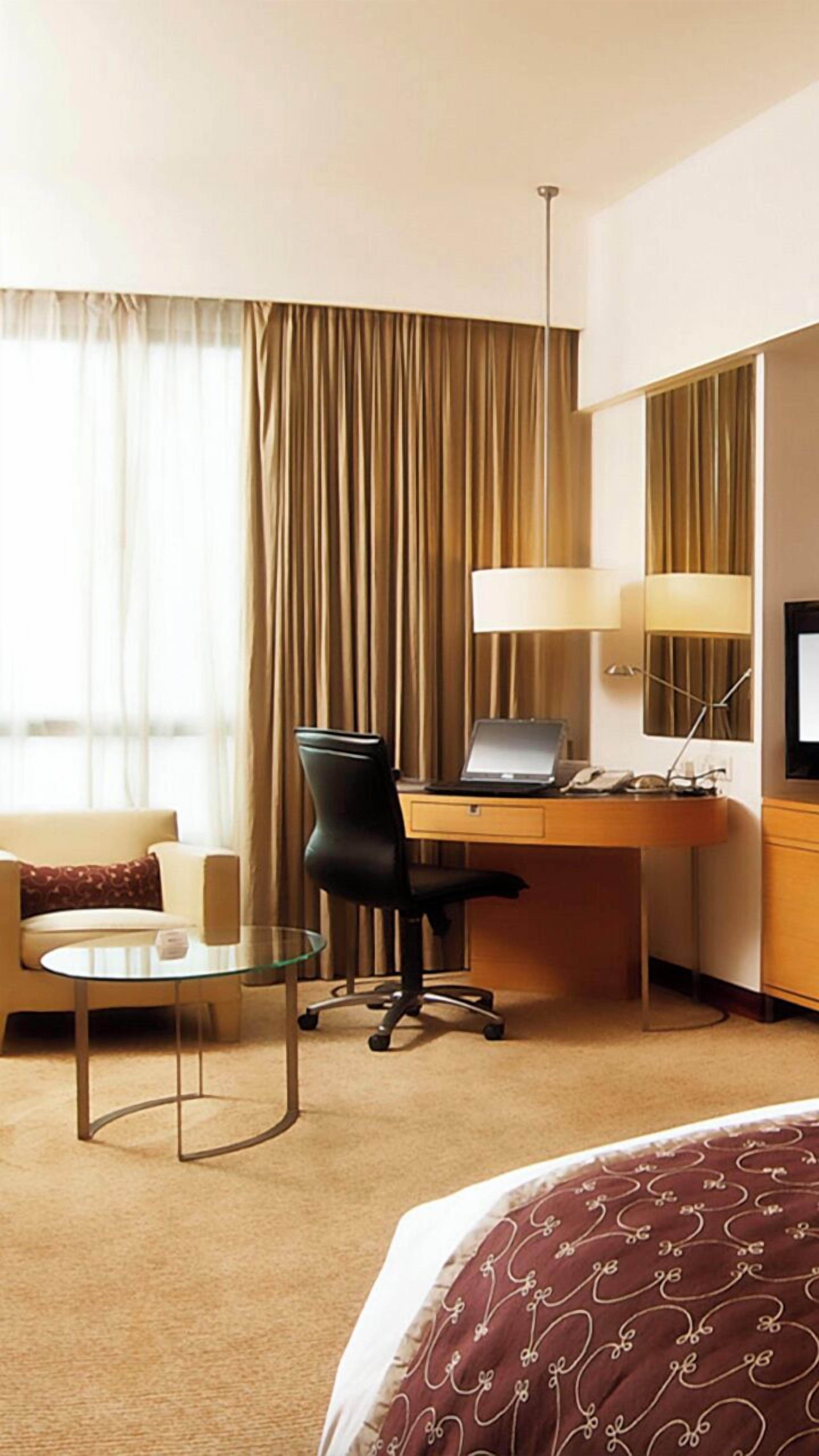 Une chambre d’hôtel comprenant un lit, un bureau avec un ordinateur portable, une chaise, une petite table, une lampe et un téléviseur.