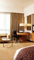 A hotel room with a bed, a desk with a laptop, a chair, a small table, a lamp, and a television.