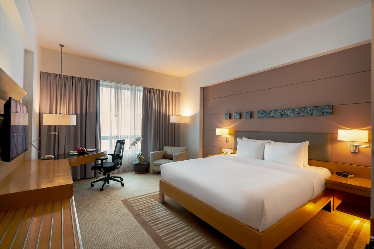 Habitación de hotel con una cama grande, un escritorio con una silla, un televisor y una lámpara.