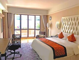 Habitación de hotel con cama, escritorio, silla, ventana grande y un reloj en la pared.