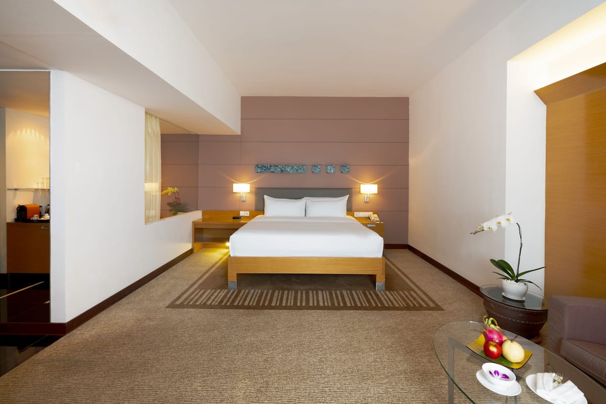 Habitación de hotel con cama, lámparas de noche, una mesita de vidrio con fruta, una orquídea en maceta y un espejo.