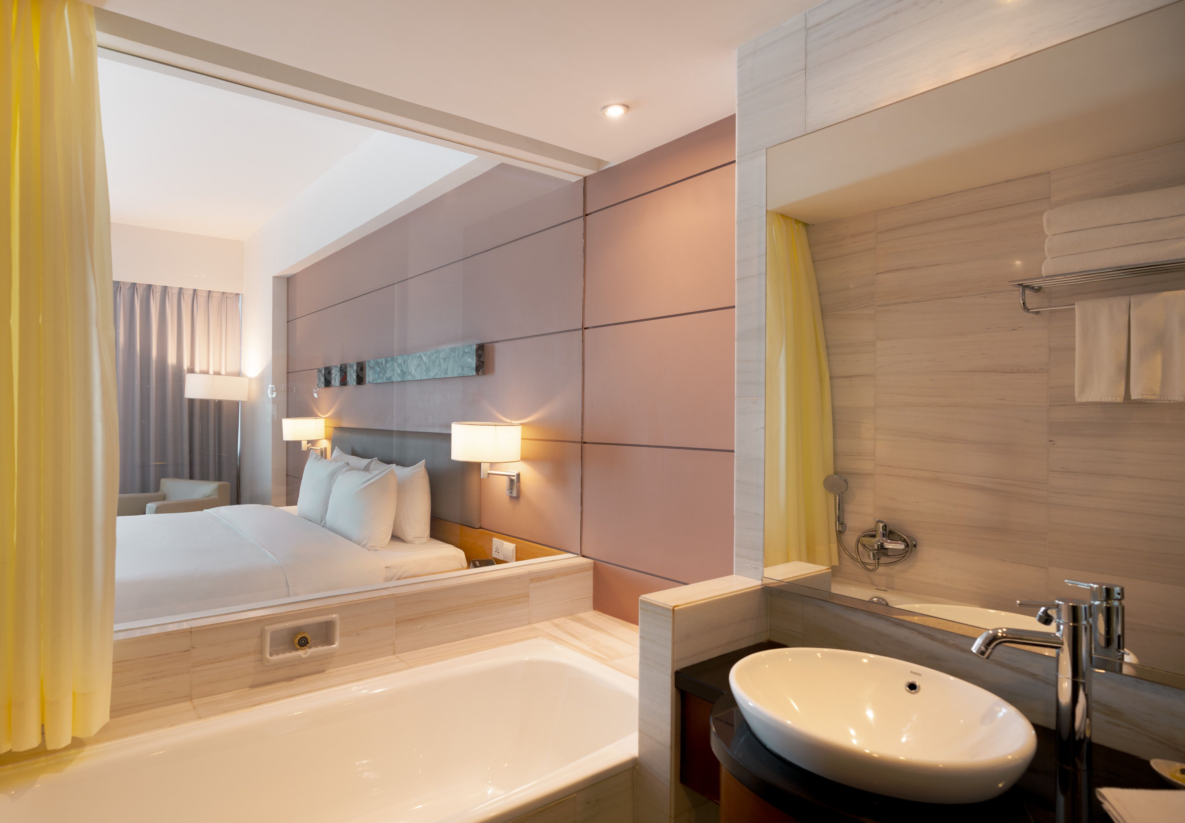 A modern hotel room with a large bed, a bathtub, a vanity with a mirror, and a view of the room's interior.