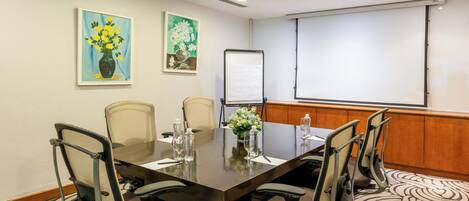 A conference room with a large table, six chairs, a projector screen, and two paintings on the wall.