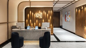 Un comptoir d’accueil moderne avec un panneau arrière en bois, un écran numérique et deux chaises noires.
