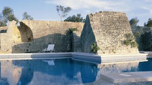 A swimming pool with a geometric tile border, a white lounge chair, and a stone wall in the background. - Casal Santa Eulàlia Hotel (Santa Margalida)