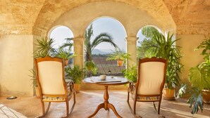 An outdoor patio with a round table and two chairs, surrounded by potted plants and an arched stone structure. - Casal Santa Eulàlia Hotel (Santa Margalida)