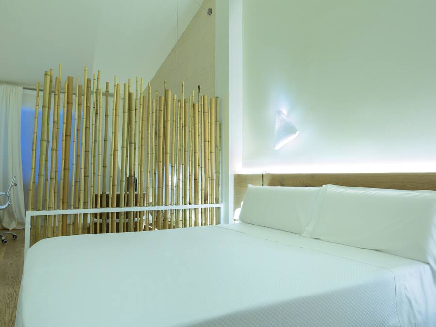 A hotel room with a large bed, a bamboo screen, a desk, and a chair.