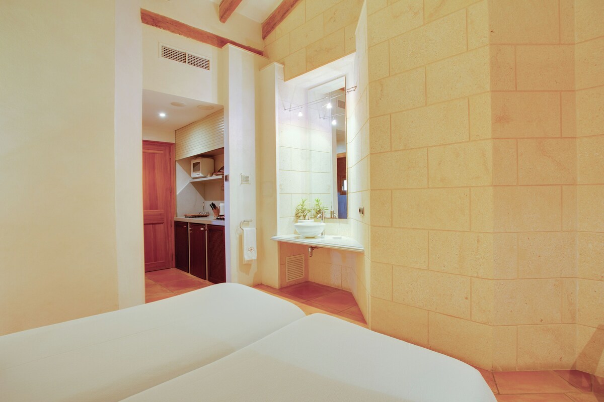 A hotel room with a bed, a bathroom with a sink and mirror, and a kitchenette area.
