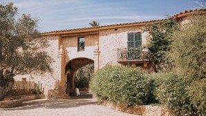 A rustic stone building with an archway entrance, a small balcony with a railing, and a stone wall with climbing plants. - Casal Santa Eulàlia Hotel (Santa Margalida)