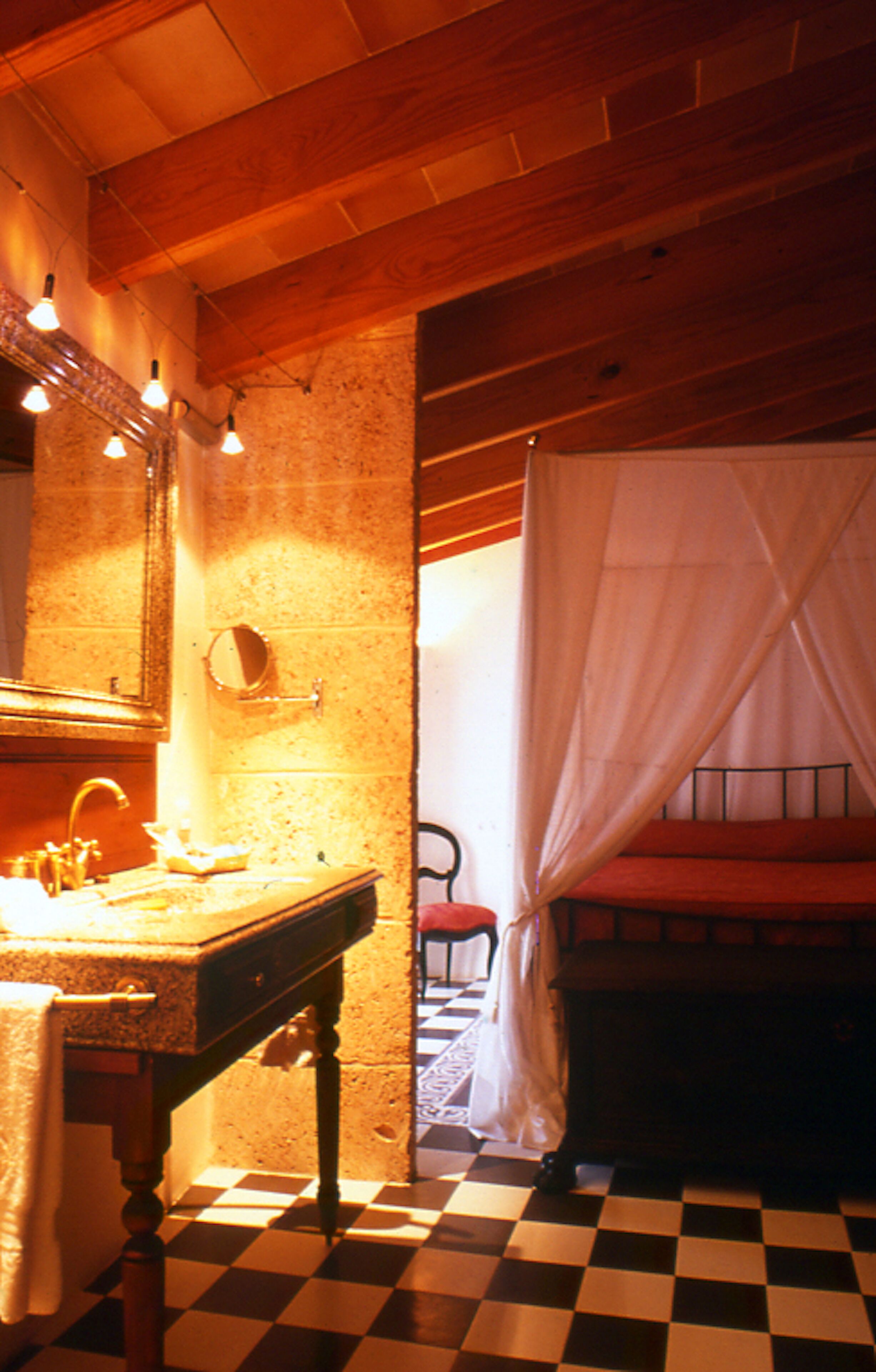 Een badkamer met een geruite vloer, een wastafel met spiegel en een bed met hemelbed.