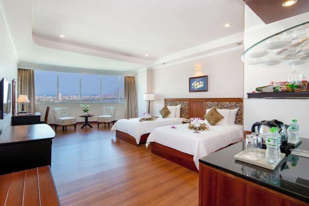Une chambre d’hôtel avec deux lits, un bureau, une chaise, une télévision et une vue sur la ville.