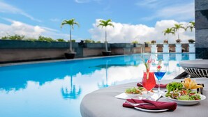 A poolside dining area with a table set for two, featuring a salad, drinks, and a bowl of fries. - Muong Thanh Luxury Song Han Hotel (Da Nang)