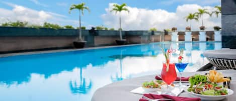 Zona de comedor junto a la piscina, con una mesa dispuesta para dos, ensalada, bebidas y un bol de papas fritas.