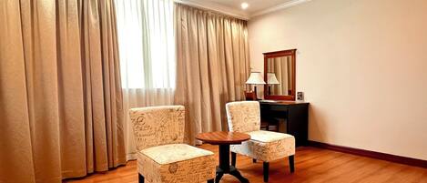 A hotel room with two armchairs, a small table, a desk with a lamp, and a mirror on the wall.