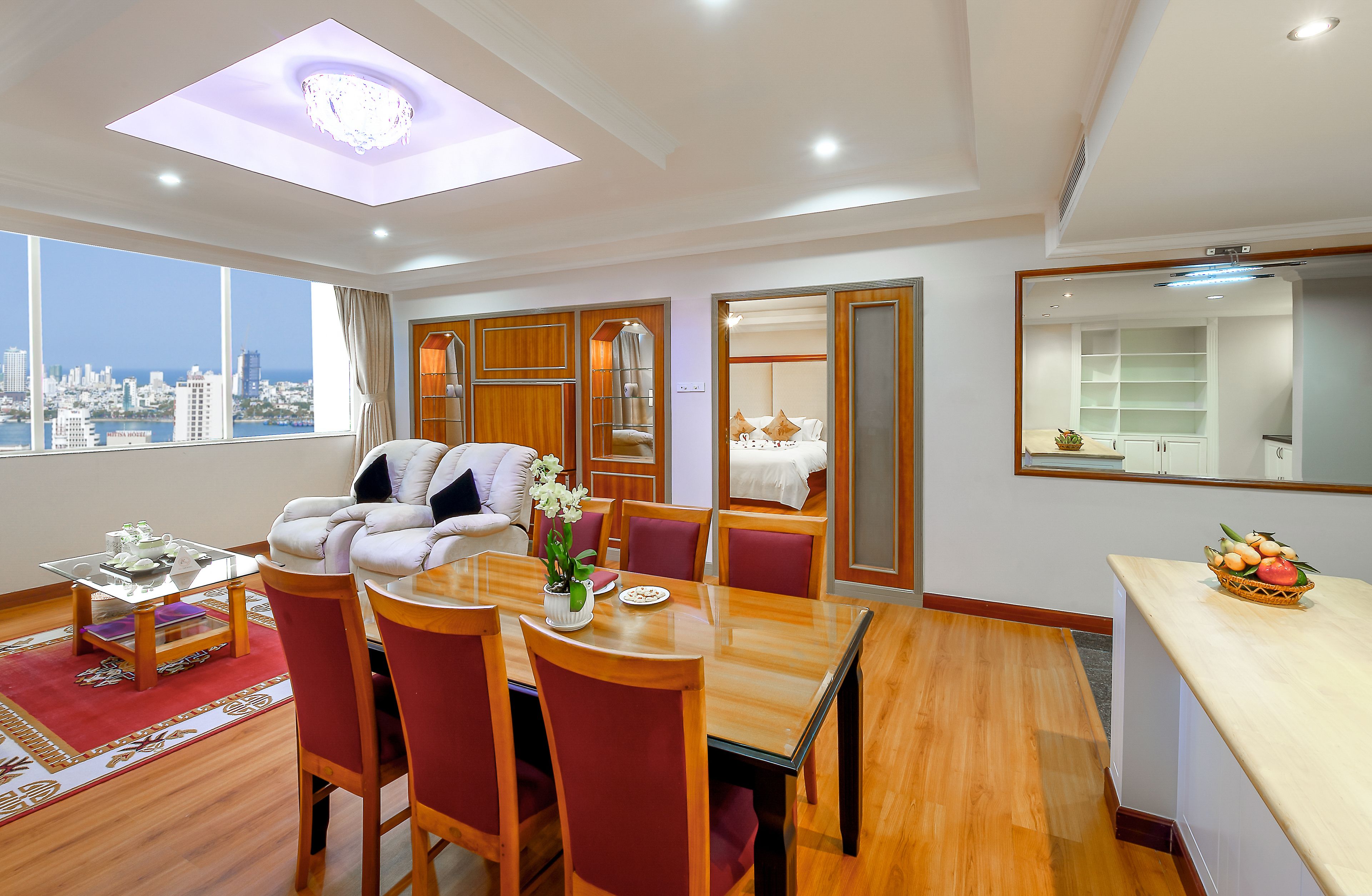 A modern hotel room with a dining area, a sitting area, and a large window offering a city view.
