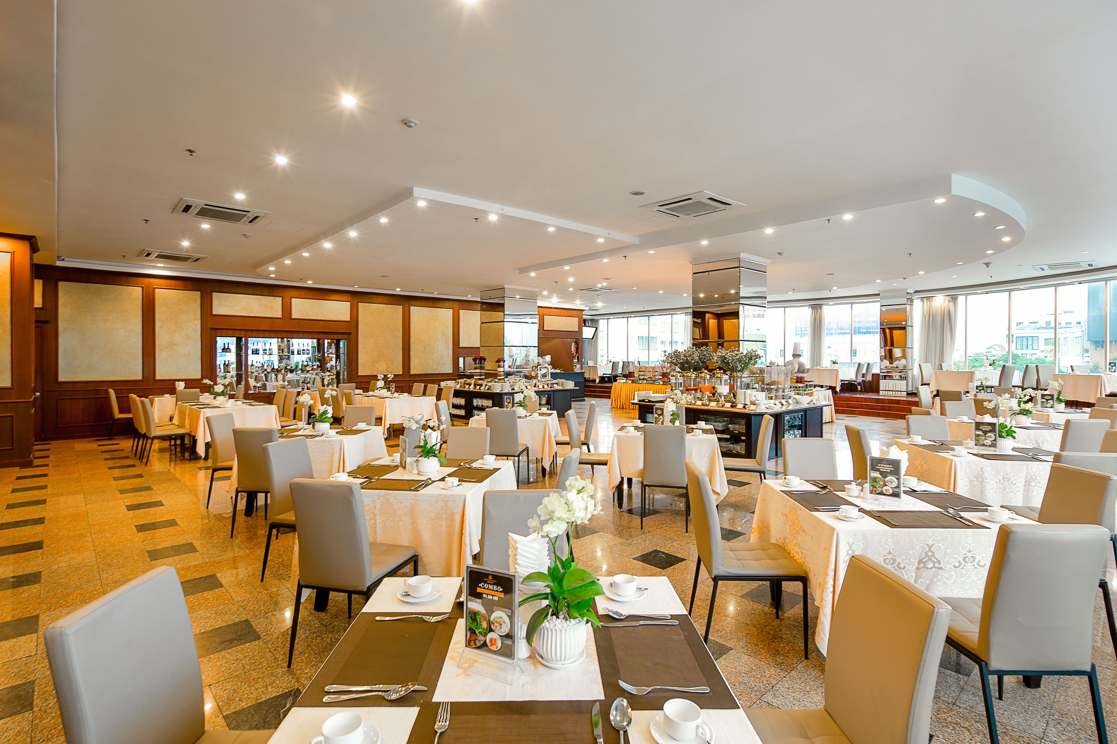 Amplio comedor de hotel con numerosas mesas y sillas, un bar y grandes ventanales con vistas a la ciudad.
