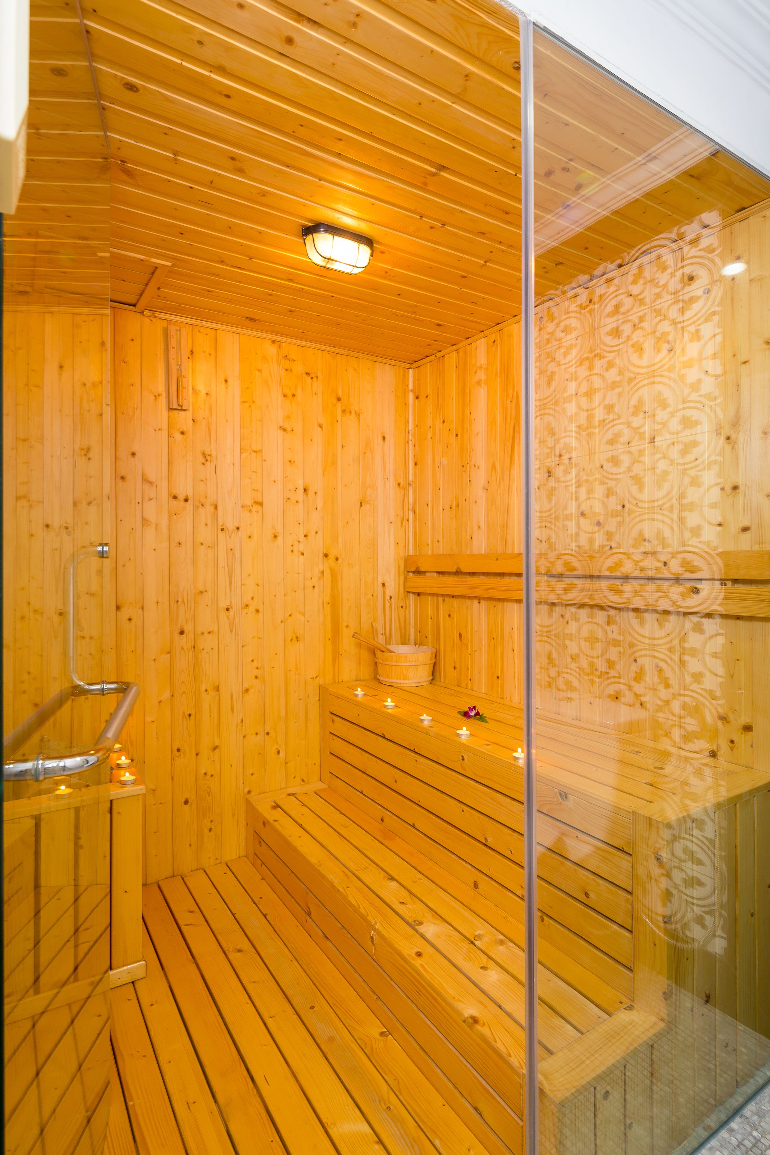 A wooden sauna with a glass partition, a bench, and a small table with candles.