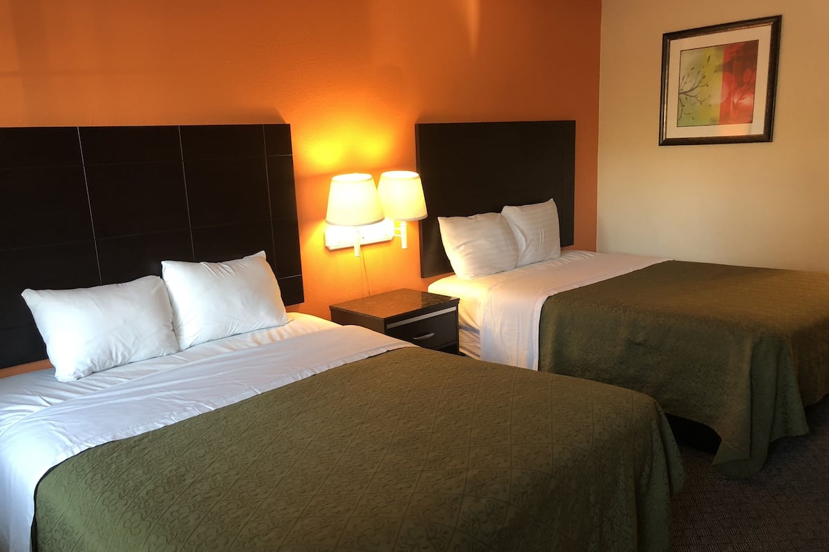 A hotel room with two single beds, a nightstand with a lamp, and a framed picture on the wall.