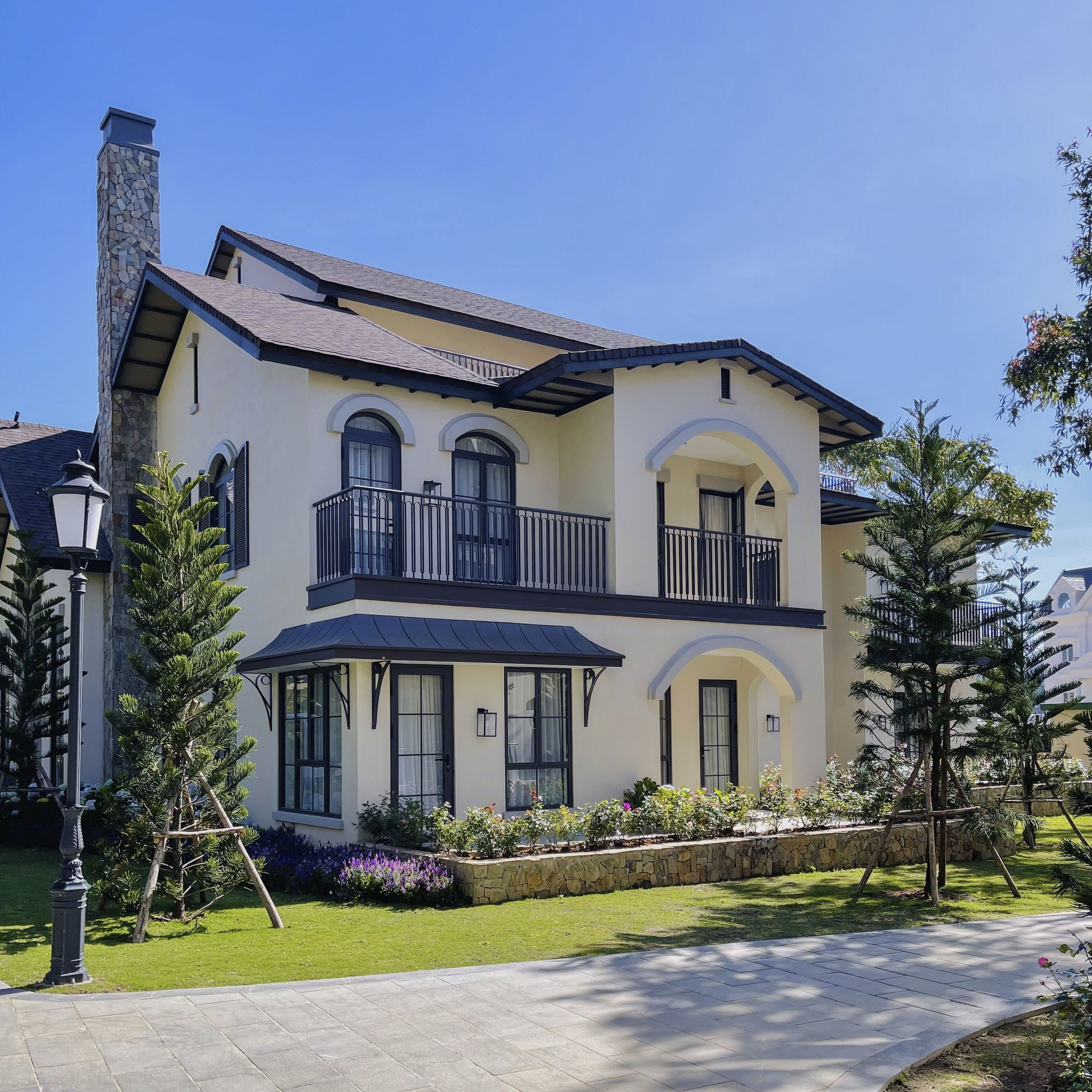 A two-story house with a stone chimney, a balcony with black railings, and a well-maintained lawn.