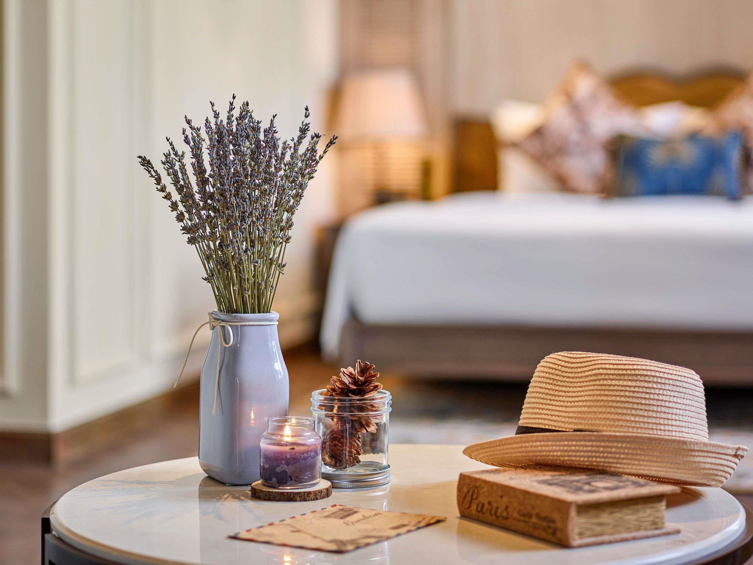 A round table with a vase of lavender, a candle, a small glass jar with pinecones, a straw hat, and a book with the word 'Paris' on it.