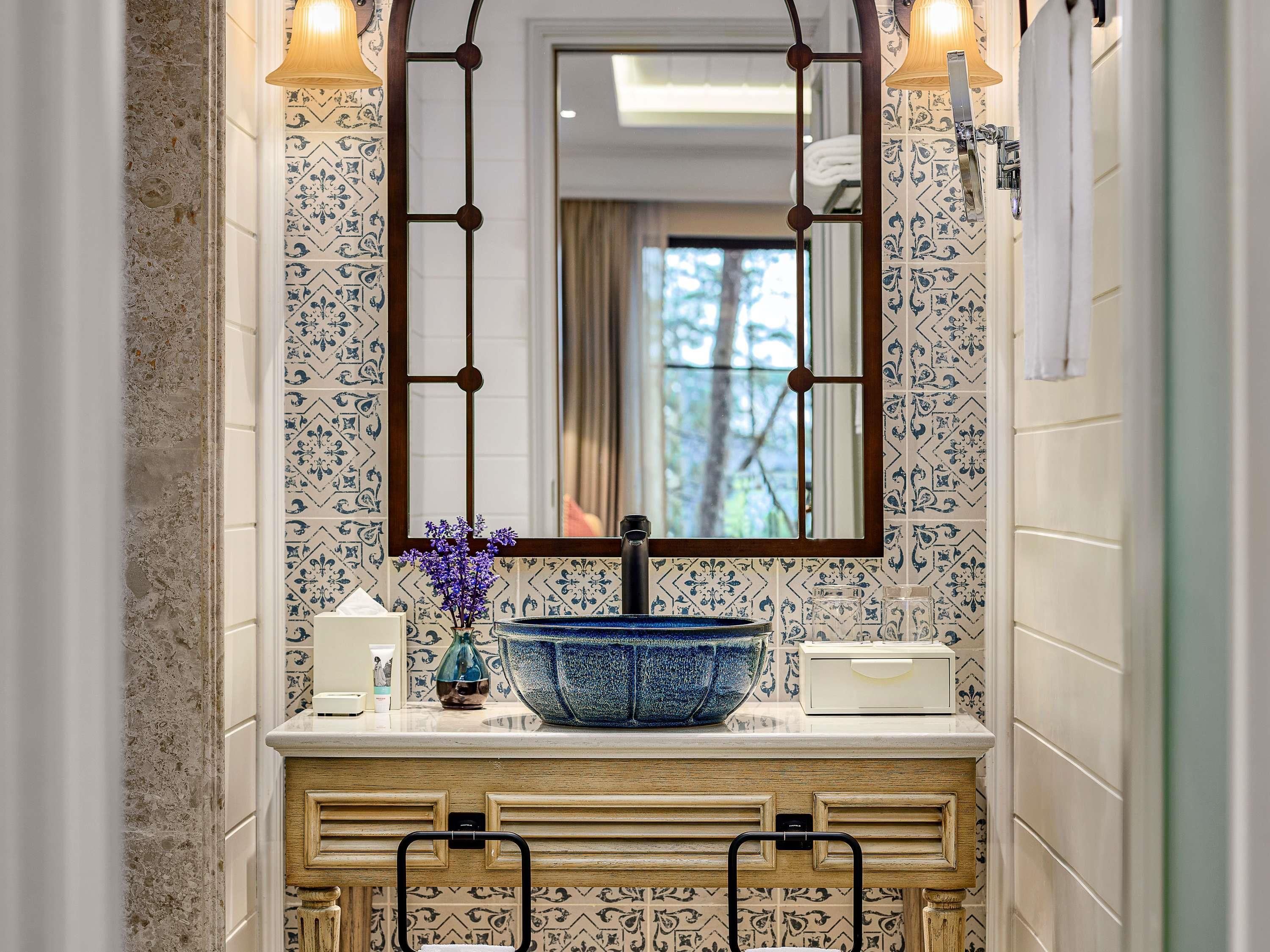 A bathroom with a large mirror, a blue ceramic sink, and patterned tiles.