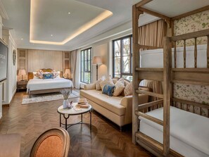 Habitación de hotel con cama, sofá, banco de madera, mesa redonda y una ventana grande.