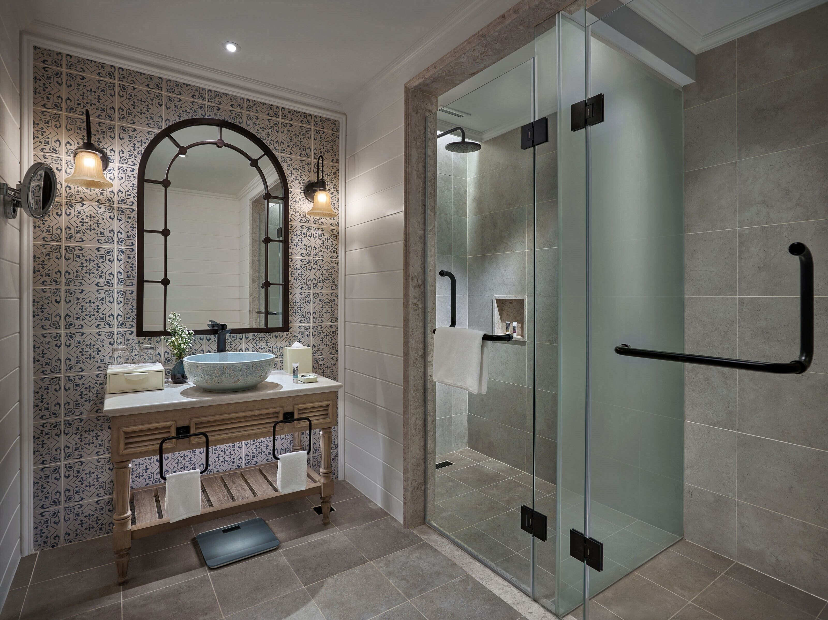 Un baño moderno con un lavamanos independiente, un espejo grande y una zona de ducha con cerramiento de vidrio.