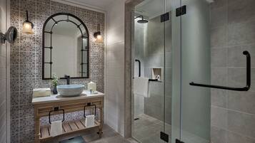 Un baño moderno con un lavamanos independiente, un espejo grande y una zona de ducha con cerramiento de vidrio.