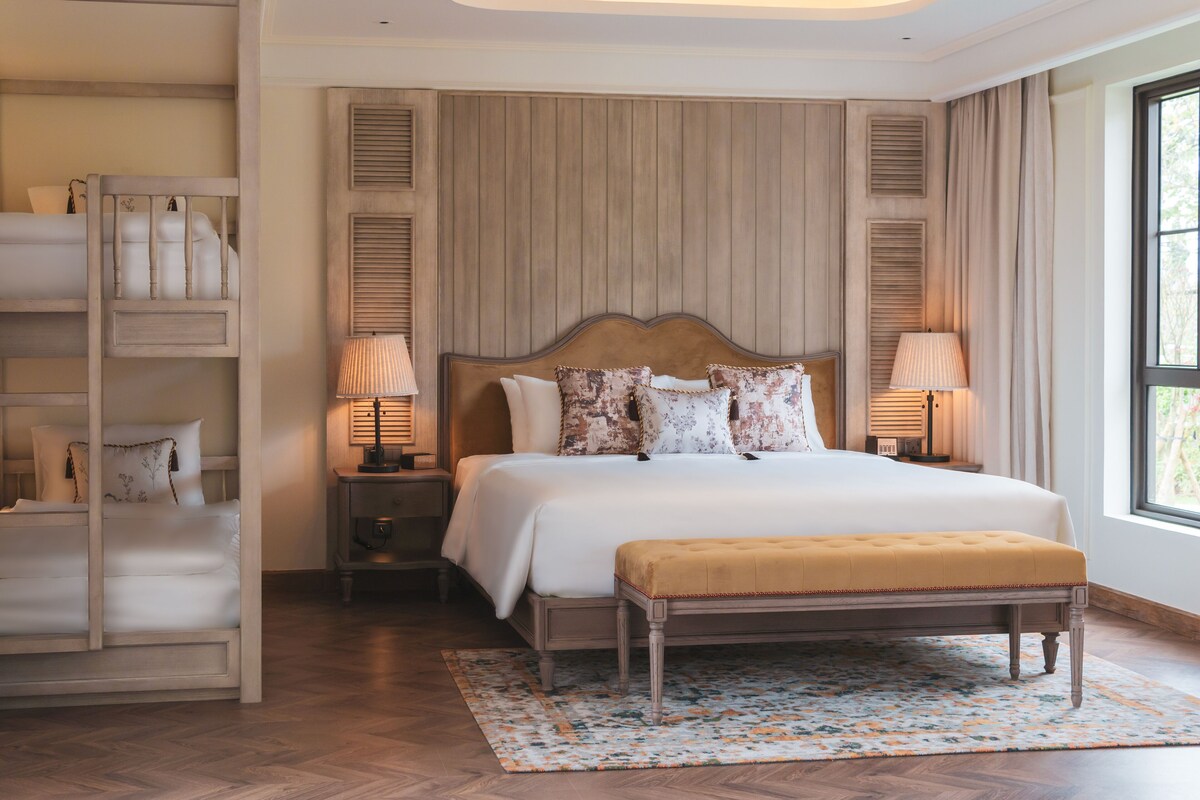 A bedroom with a large bed, a wooden bench, a nightstand, and a built-in shelving unit.