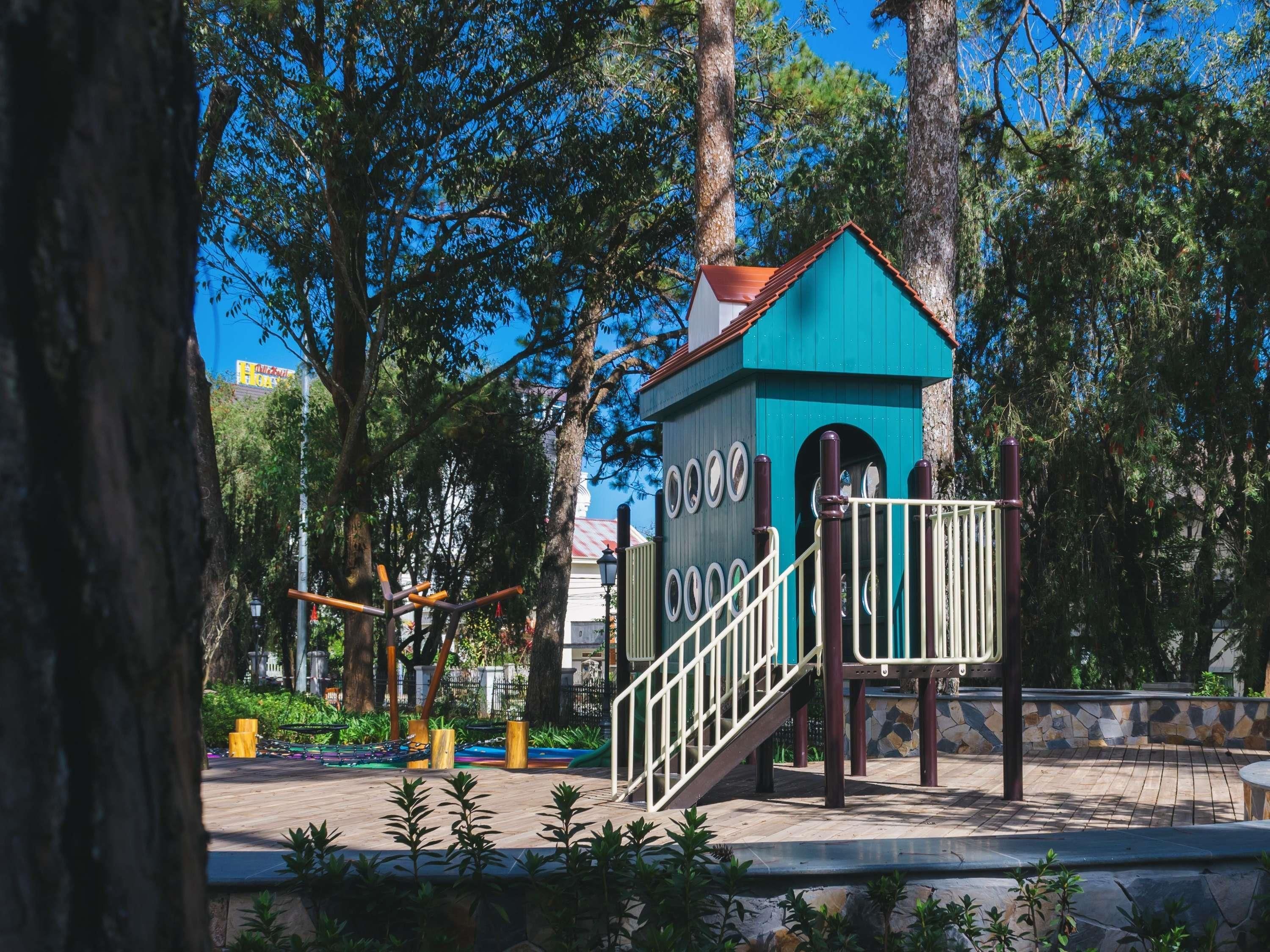 A playground with a climbing structure and a small blue building with stairs.