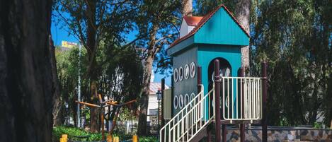 A playground with a climbing structure and a small blue building with stairs.