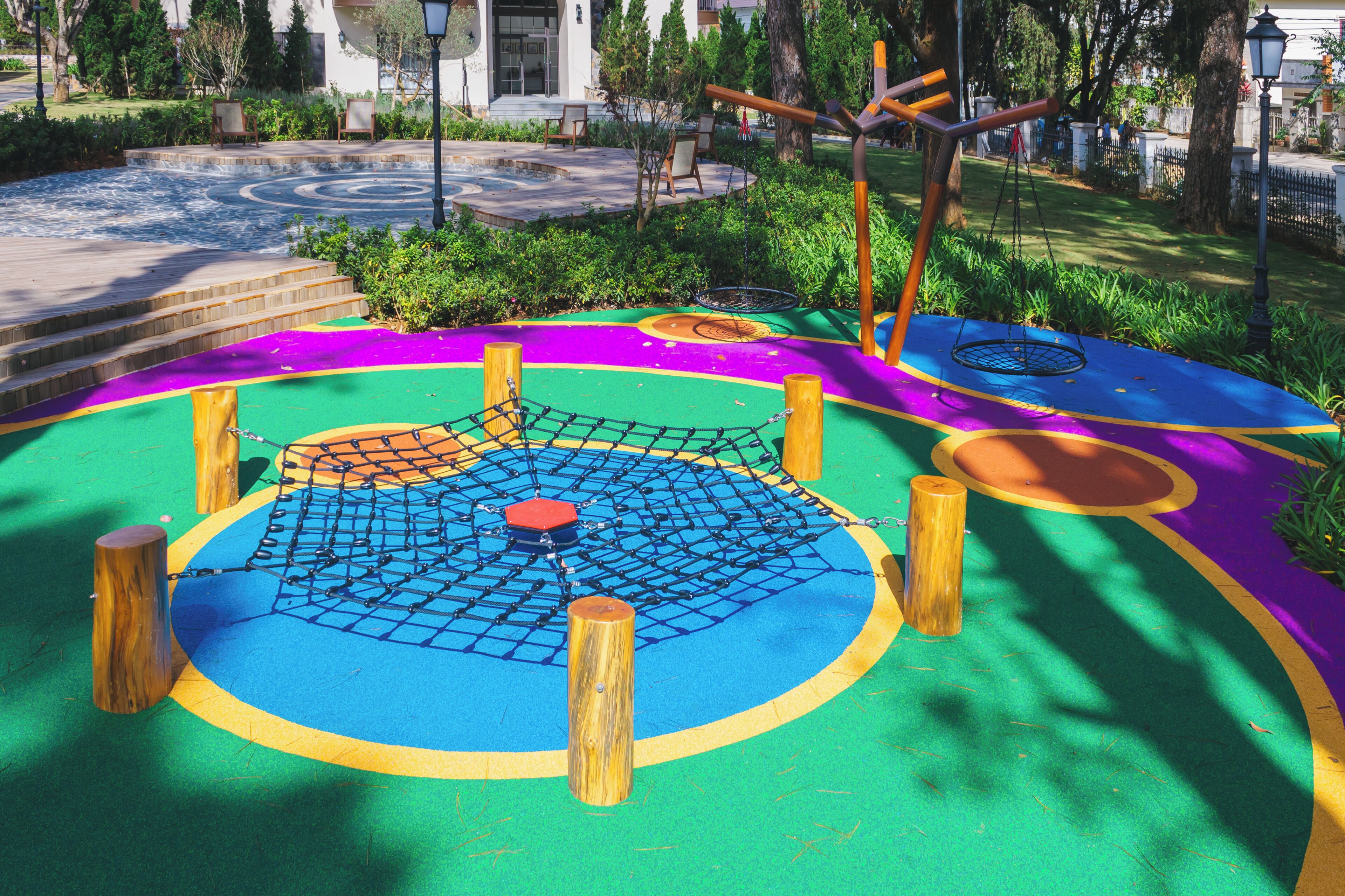 Un parque infantil con una zona de juegos colorida, que incluye una estructura de escalada con red y columpios.