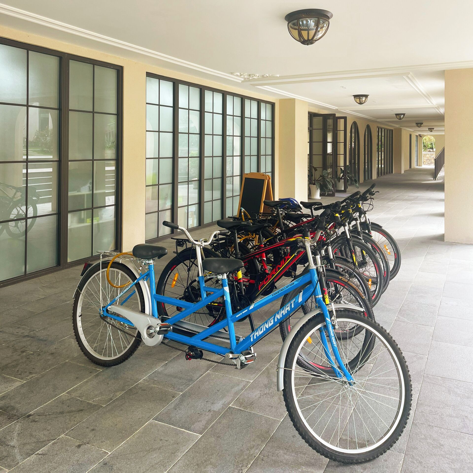 A hallway with bicycles parked along the wall, a signboard, and a staircase in the distance.