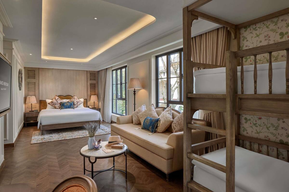 A hotel room with a bed, a sofa, a small table, and a wooden bench.