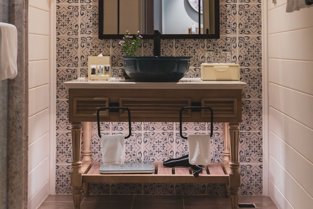 A bathroom with a large mirror, two wall-mounted lights, a sink with a basin, and a towel rack.