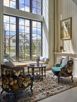 Une pièce dotée d’une grande fenêtre, d’une cheminée et de deux fauteuils rembourrés recouverts d’un tissu à motifs floraux.