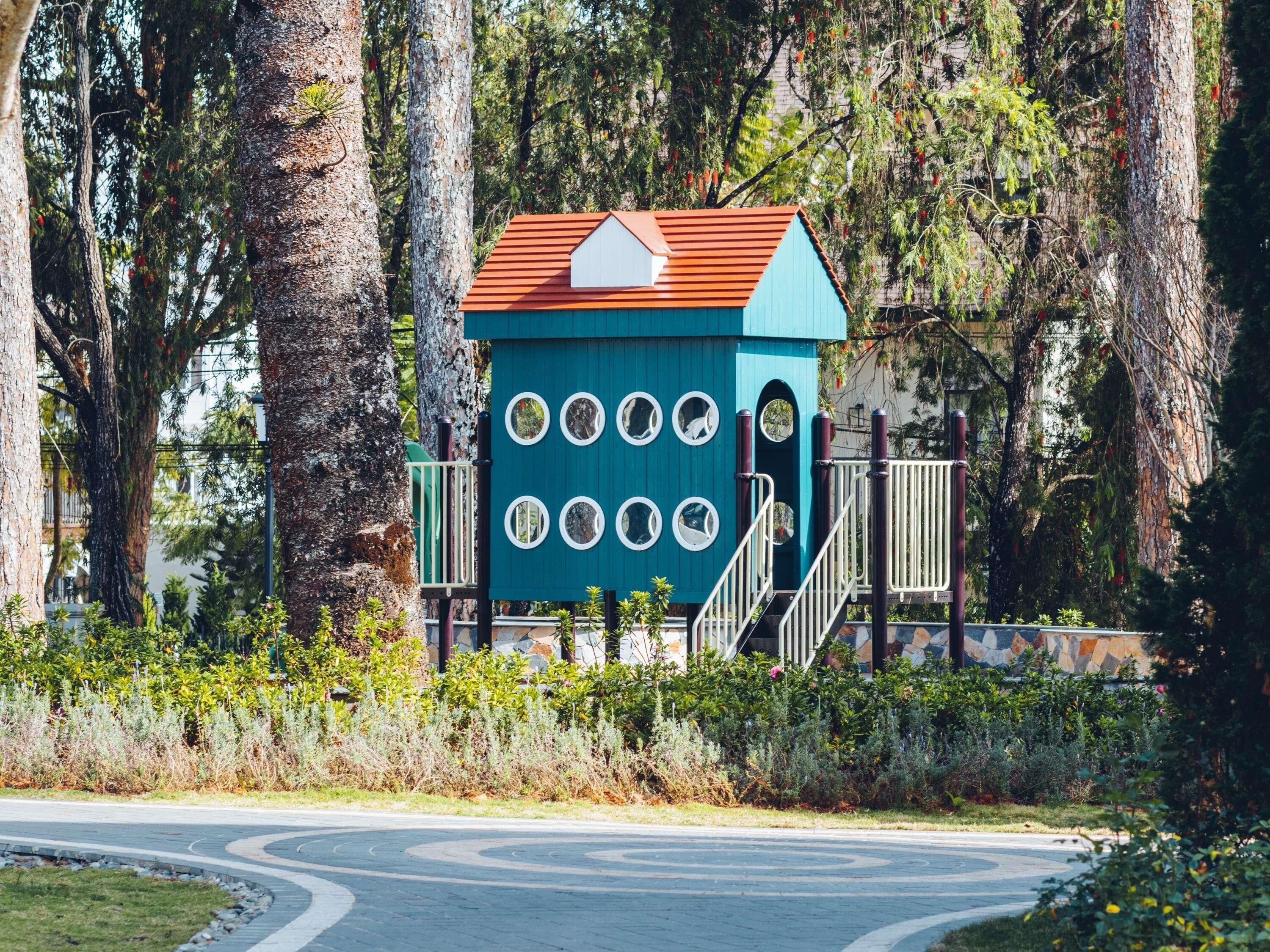 A small, blue building with a red roof, surrounded by trees and a curved road.