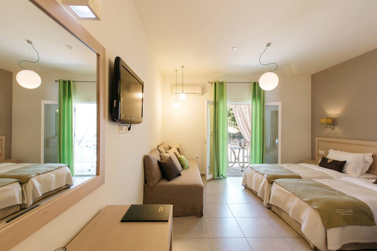 Een hotelkamer met twee eenpersoonsbedden, een slaapbank, een televisie en een tafel.