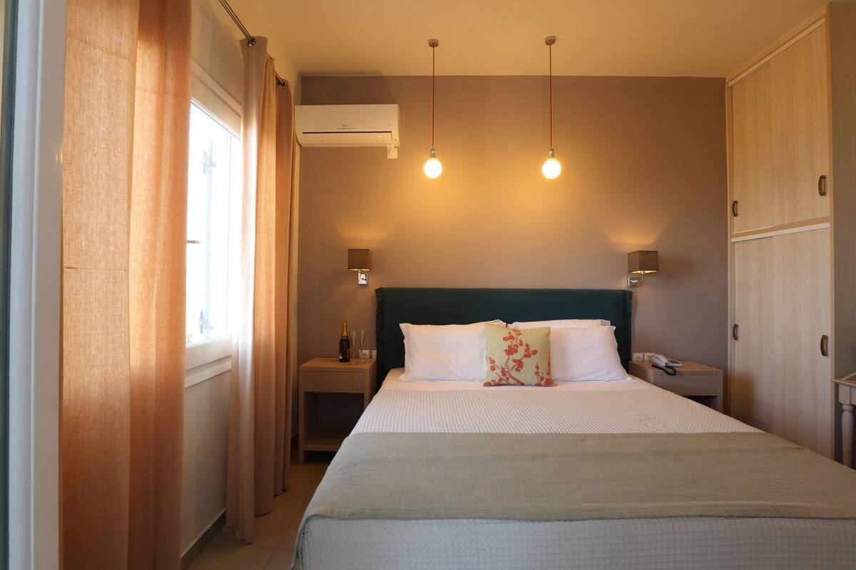 Een hotelkamer met een bed, nachtlampjes, een airconditioner en een raam met gordijnen.