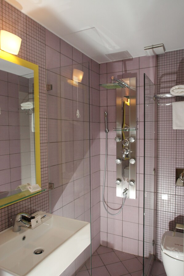 Un baño con ducha de vidrio, un lavamanos blanco y un espejo grande con marco amarillo.