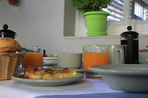 A breakfast table with a coffee maker, a glass of orange juice, a plate of food, and a green potted plant in the background.