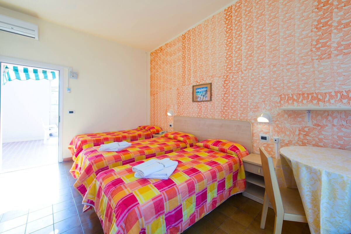 A hotel room with two beds, a small table, and a view of the outside.