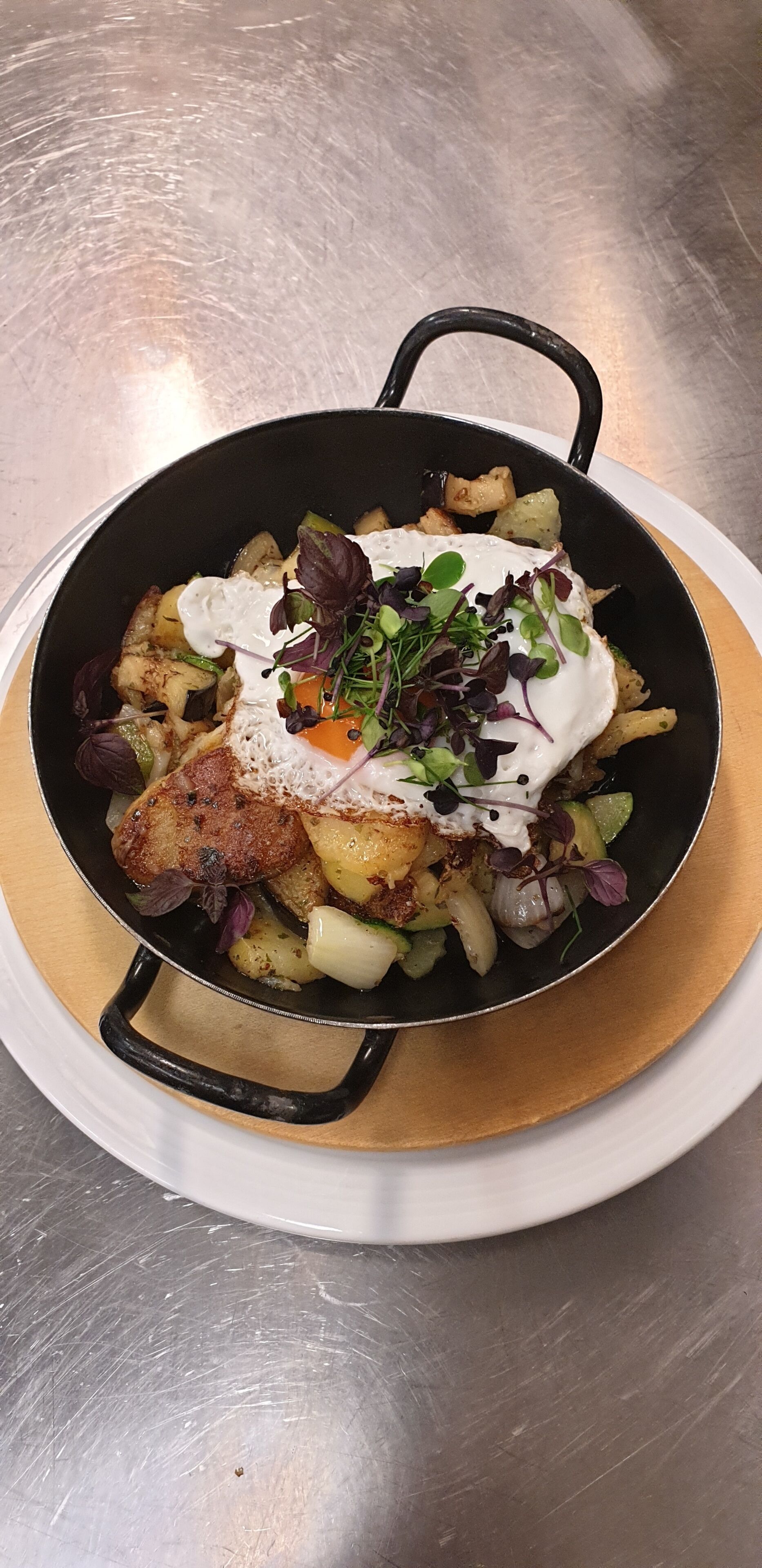 Una sartén con un plato de patatas, verduras y un huevo escalfado sobre un plato blanco.