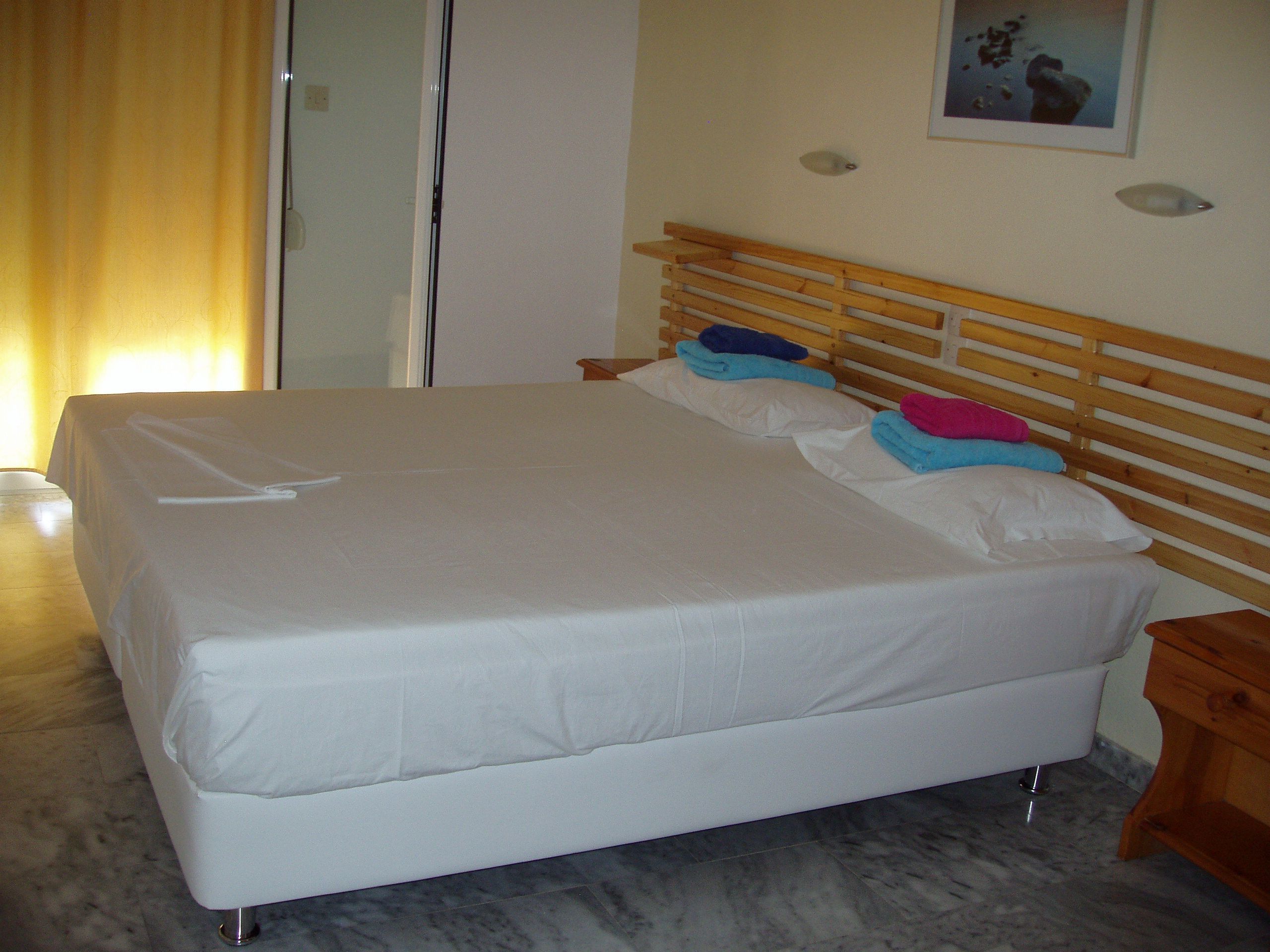 Un letto rifatto con lenzuola bianche, una testiera in legno e un pavimento in marmo.