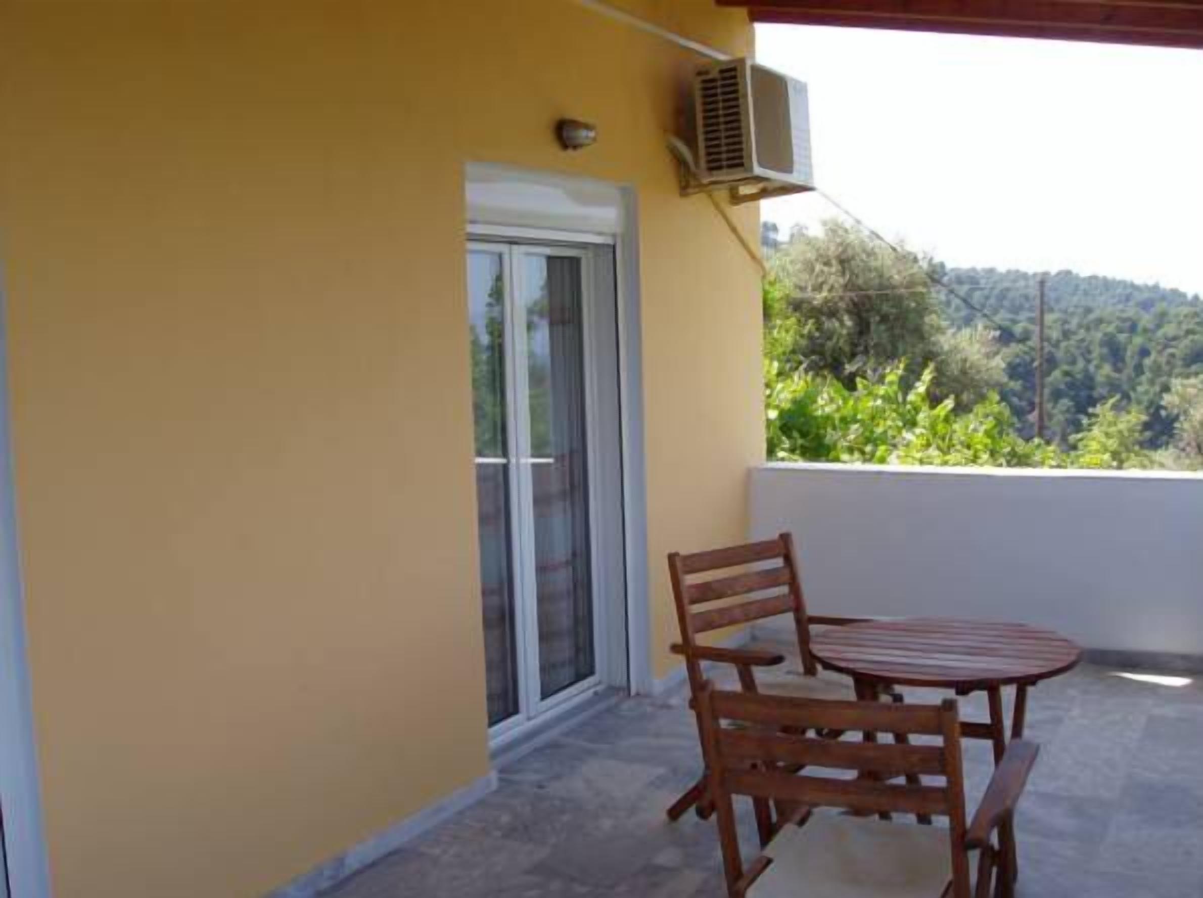 A balcony with a wooden table and chairs, a sliding glass door, and an air conditioning unit.