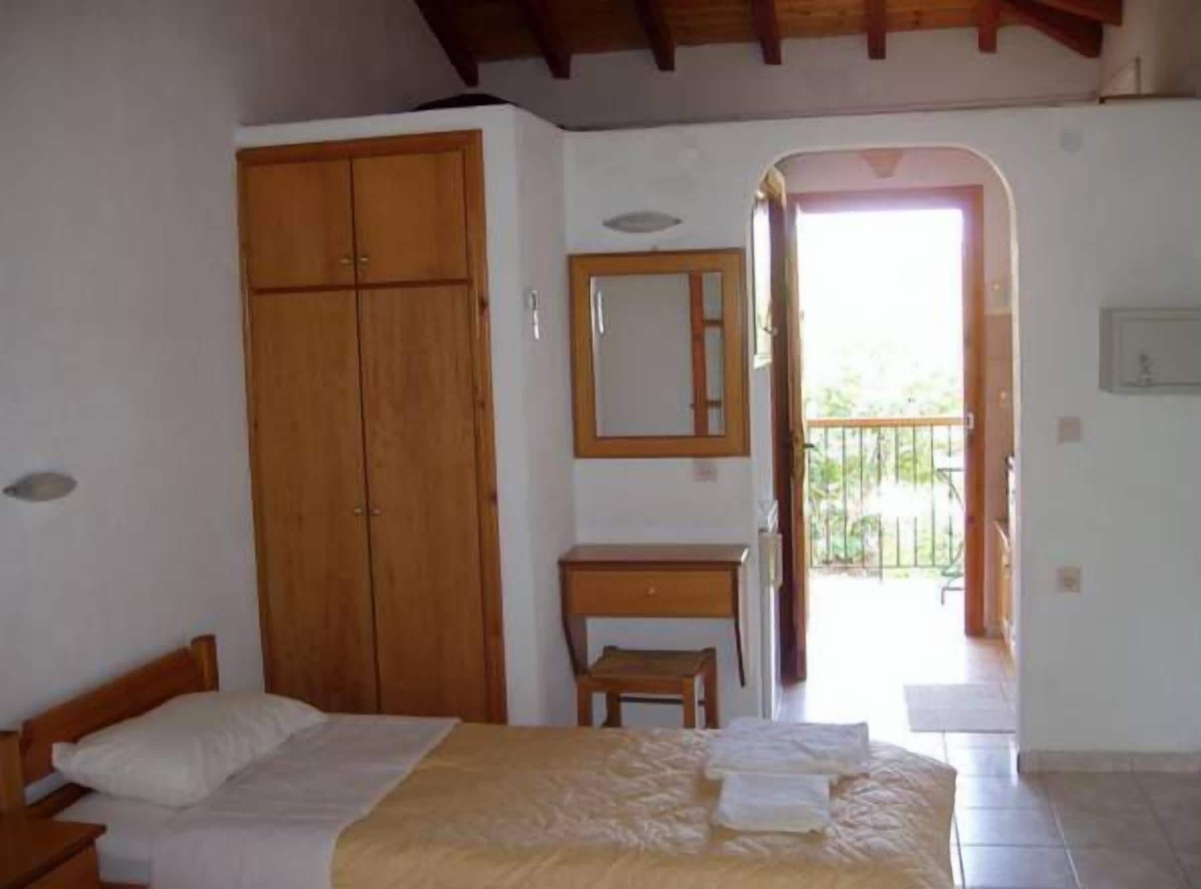 A bedroom with a bed, wooden wardrobe, a small desk, and a mirror.