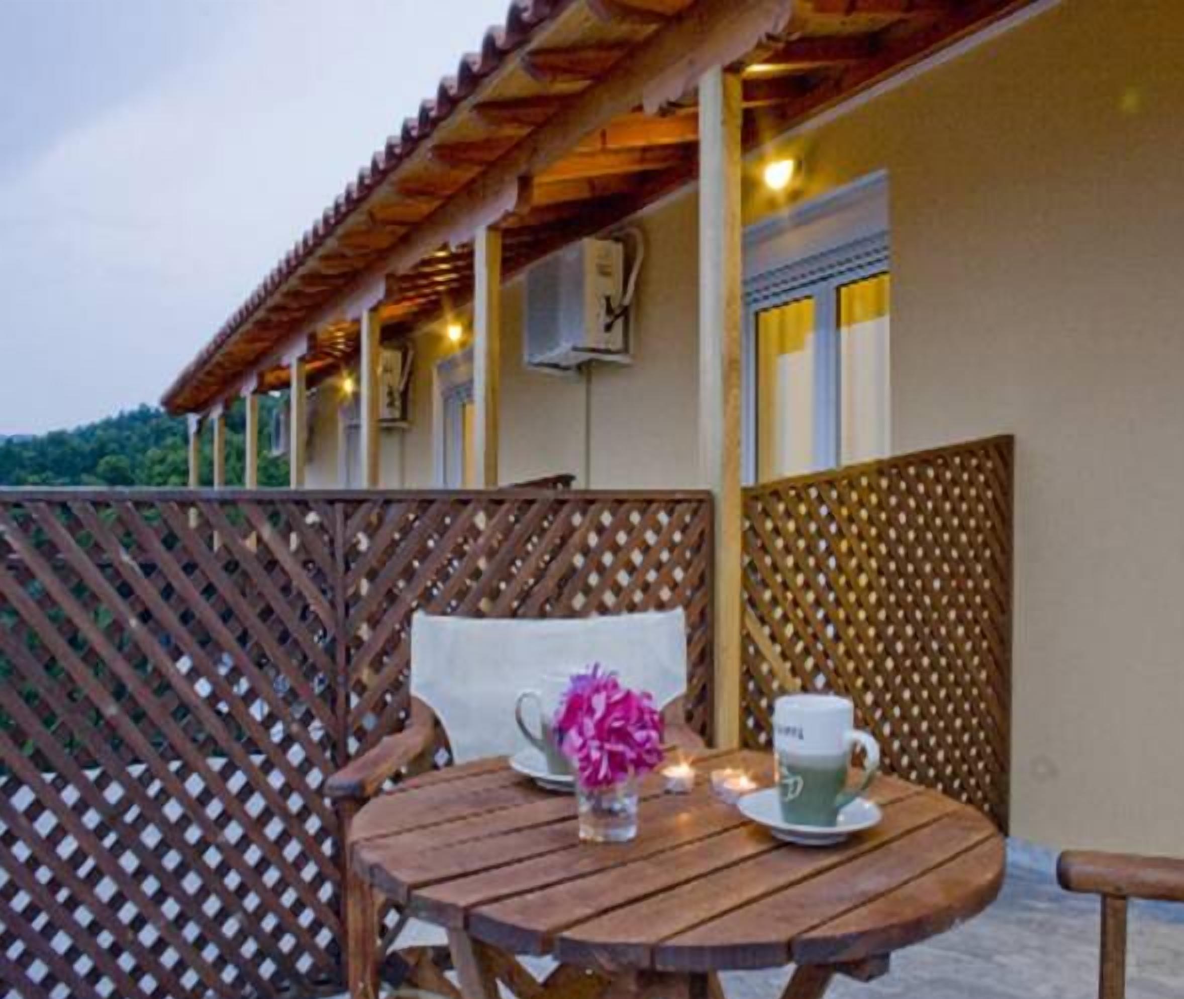 A wooden table with a cup and flowers, a wooden chair, and a wooden fence.