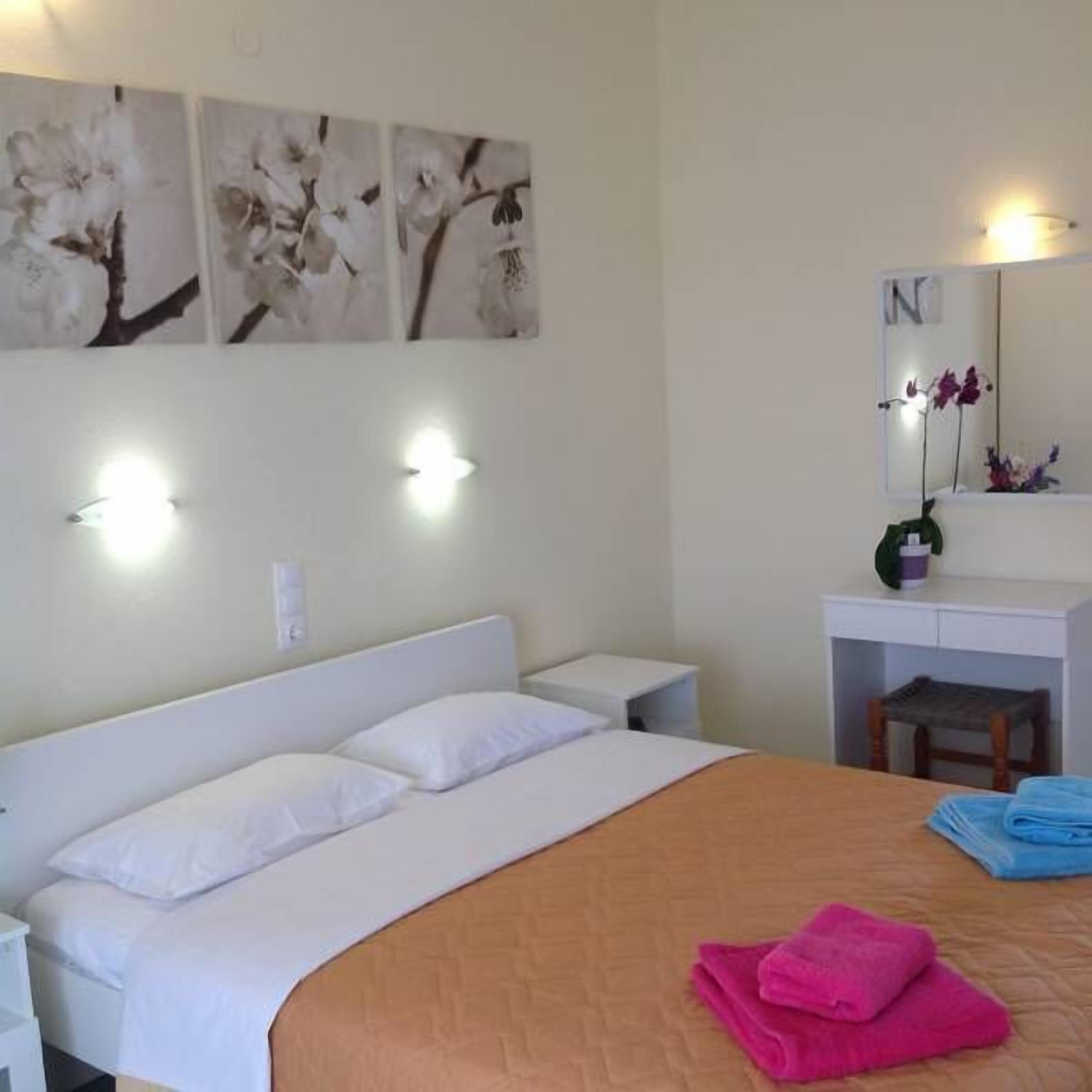 Habitación de hotel con cama, mesitas de noche blancas, un escritorio con espejo e iluminación en la pared.