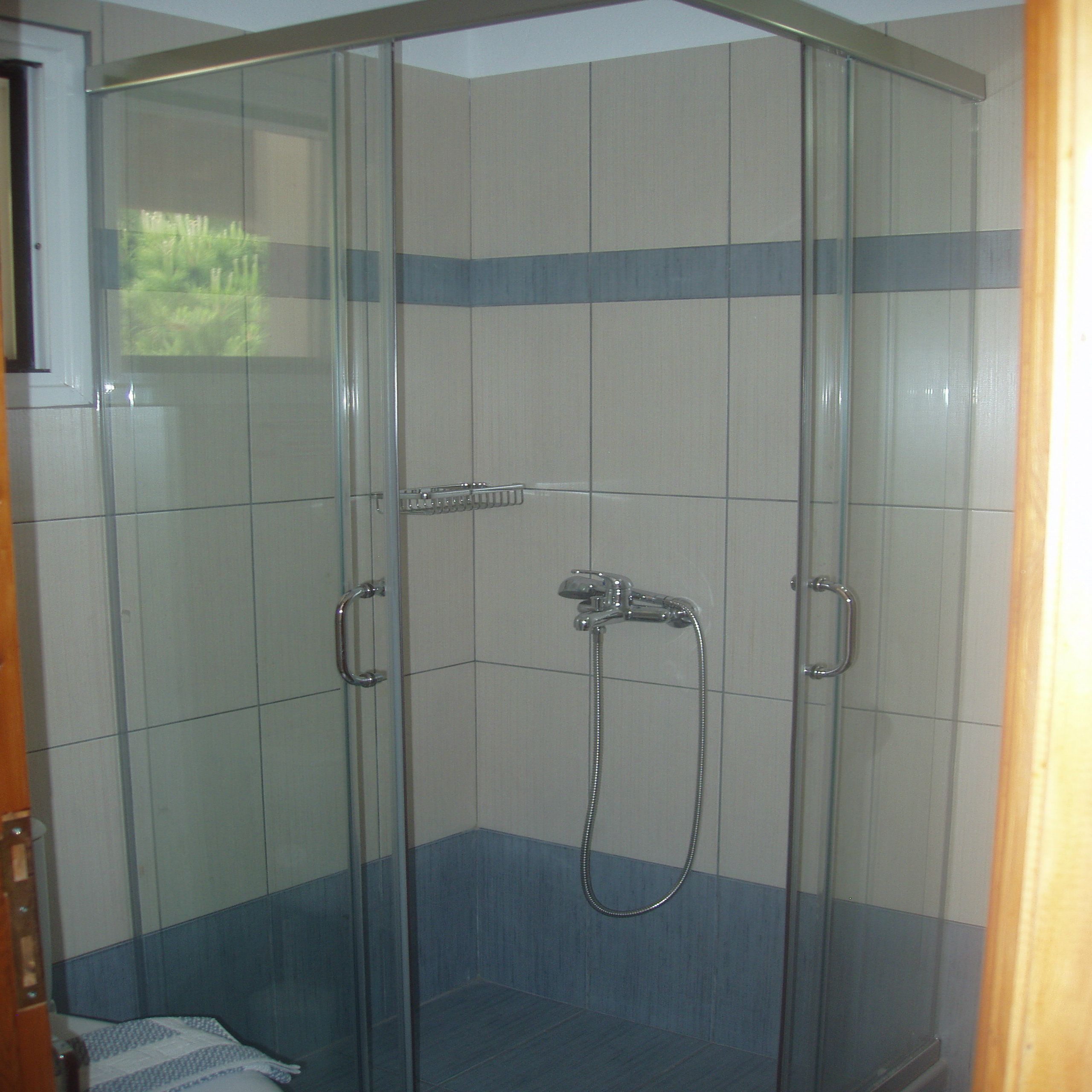 A glass-enclosed shower with a handheld showerhead and a handheld faucet.